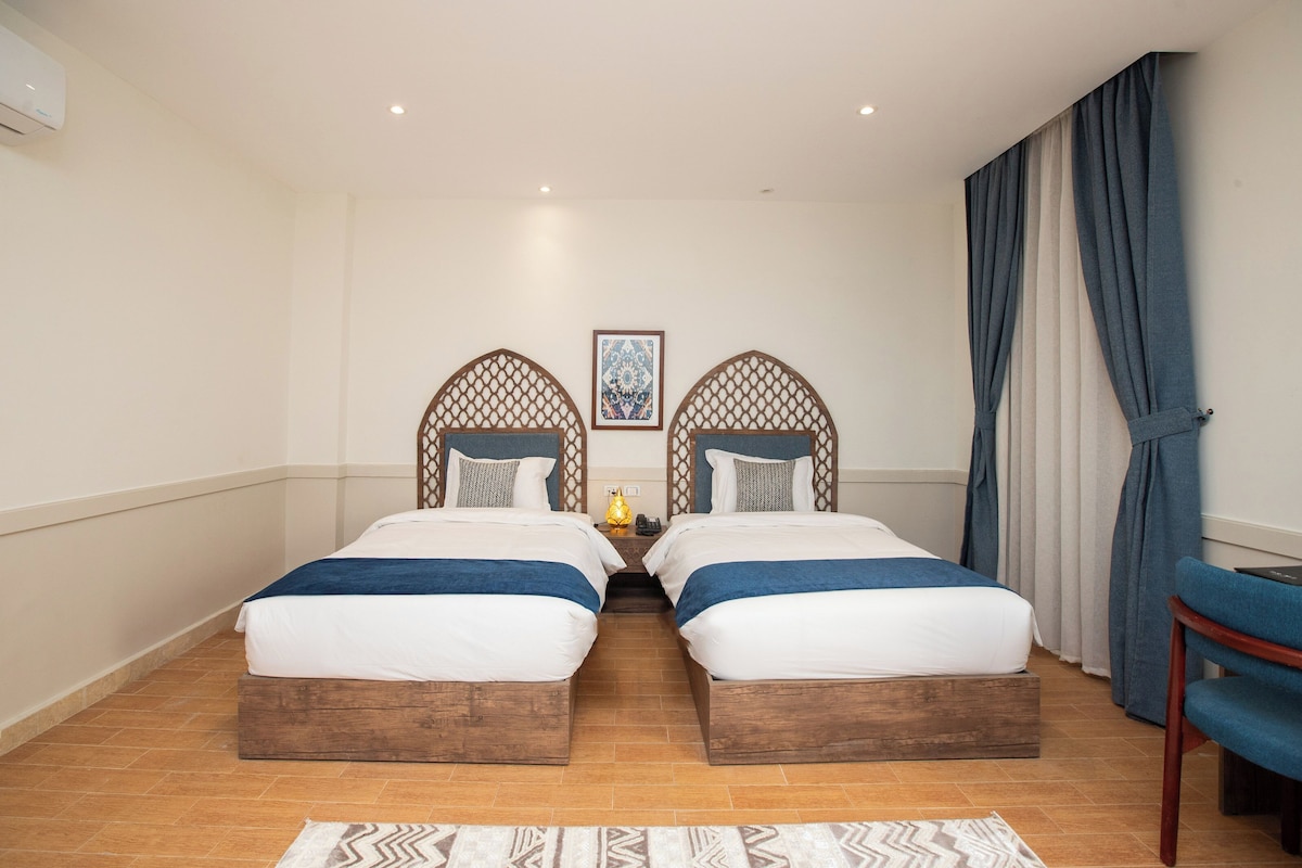 Une chambre d’hôtel avec deux lits, une tête de lit en bois, une table de chevet, une lampe et une chaise.