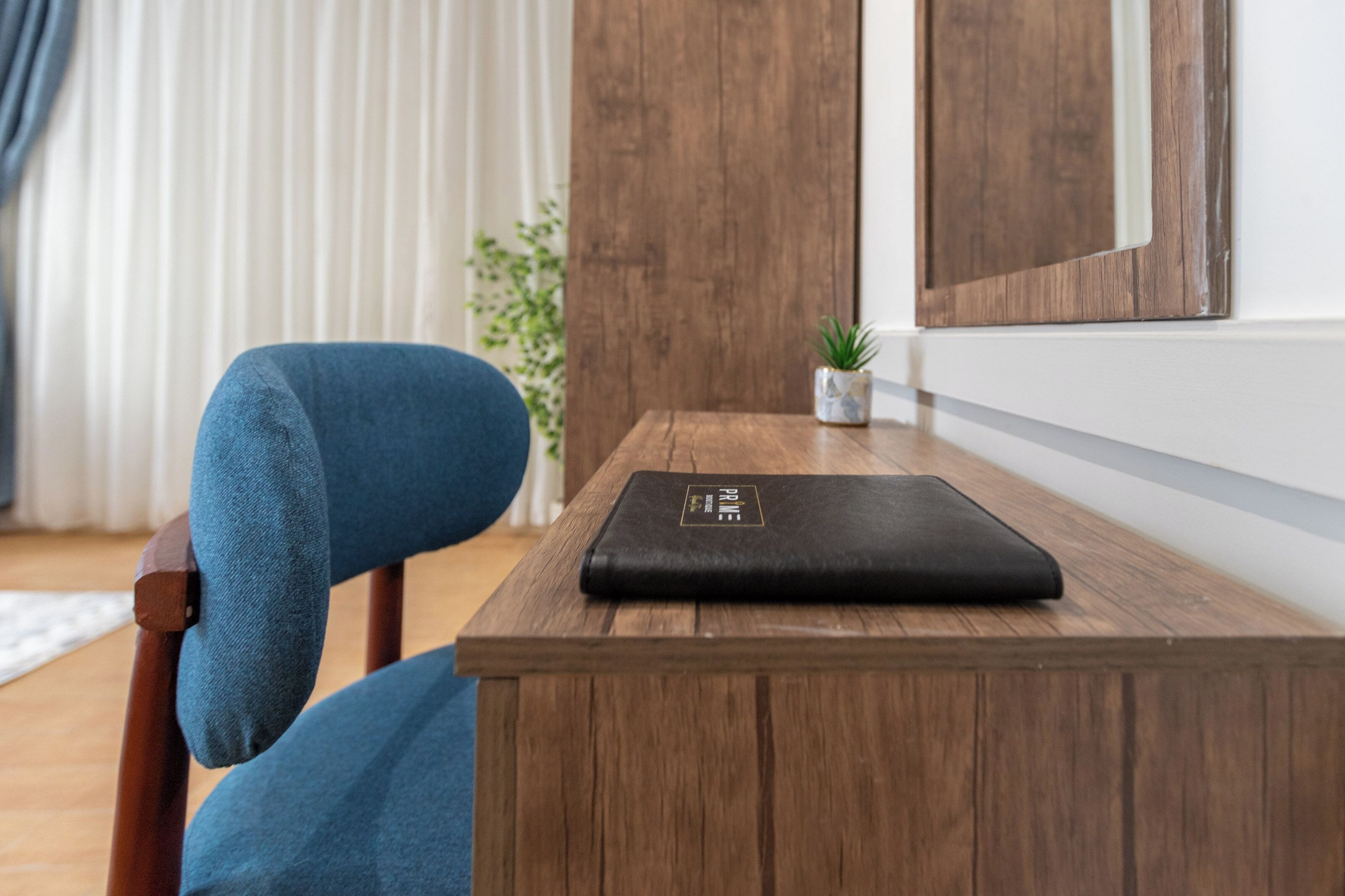 A wooden table with a black object on it, a blue chair, a small plant, and a wooden door in the background.