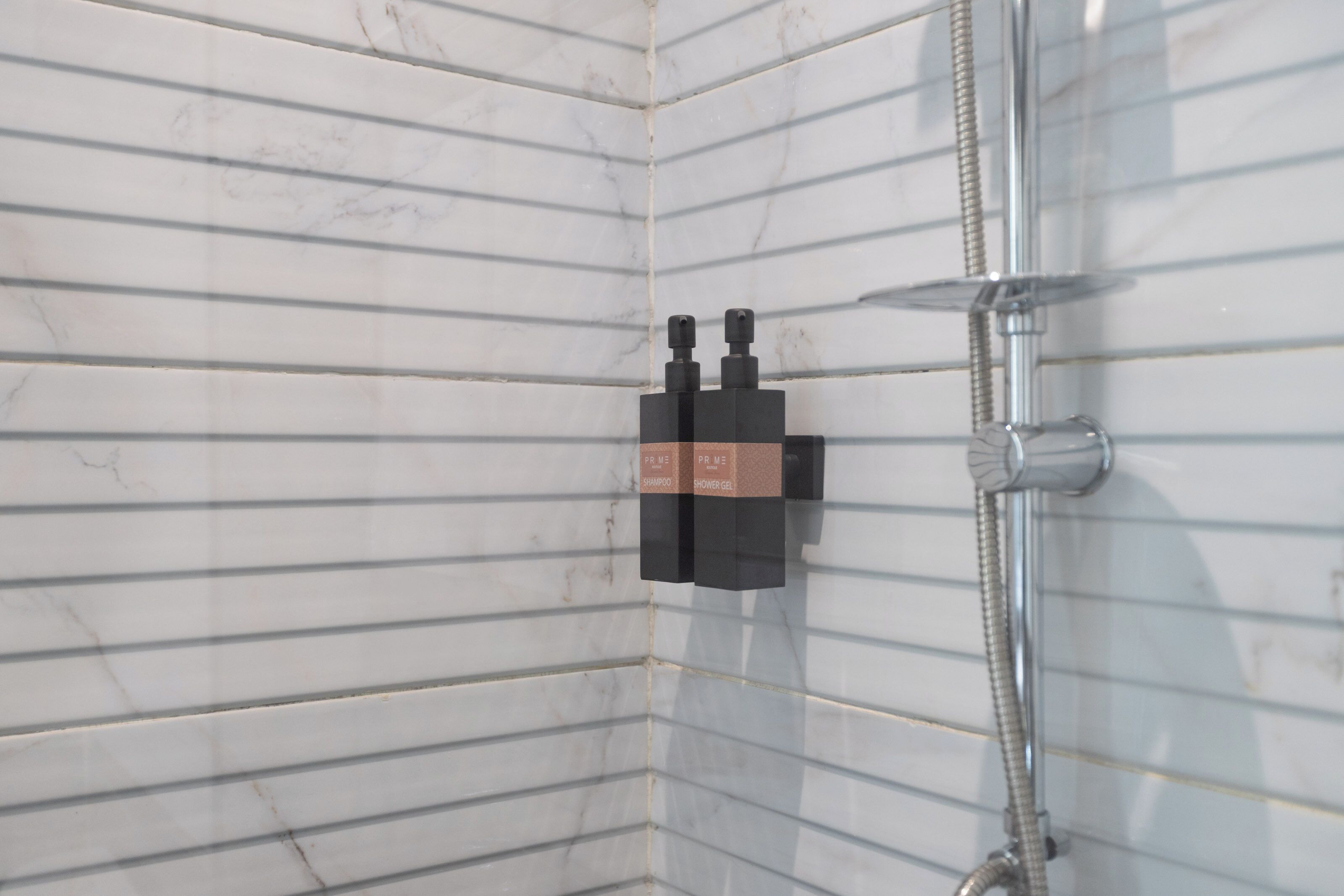 A corner of a bathroom with white tiled walls and a shower area.