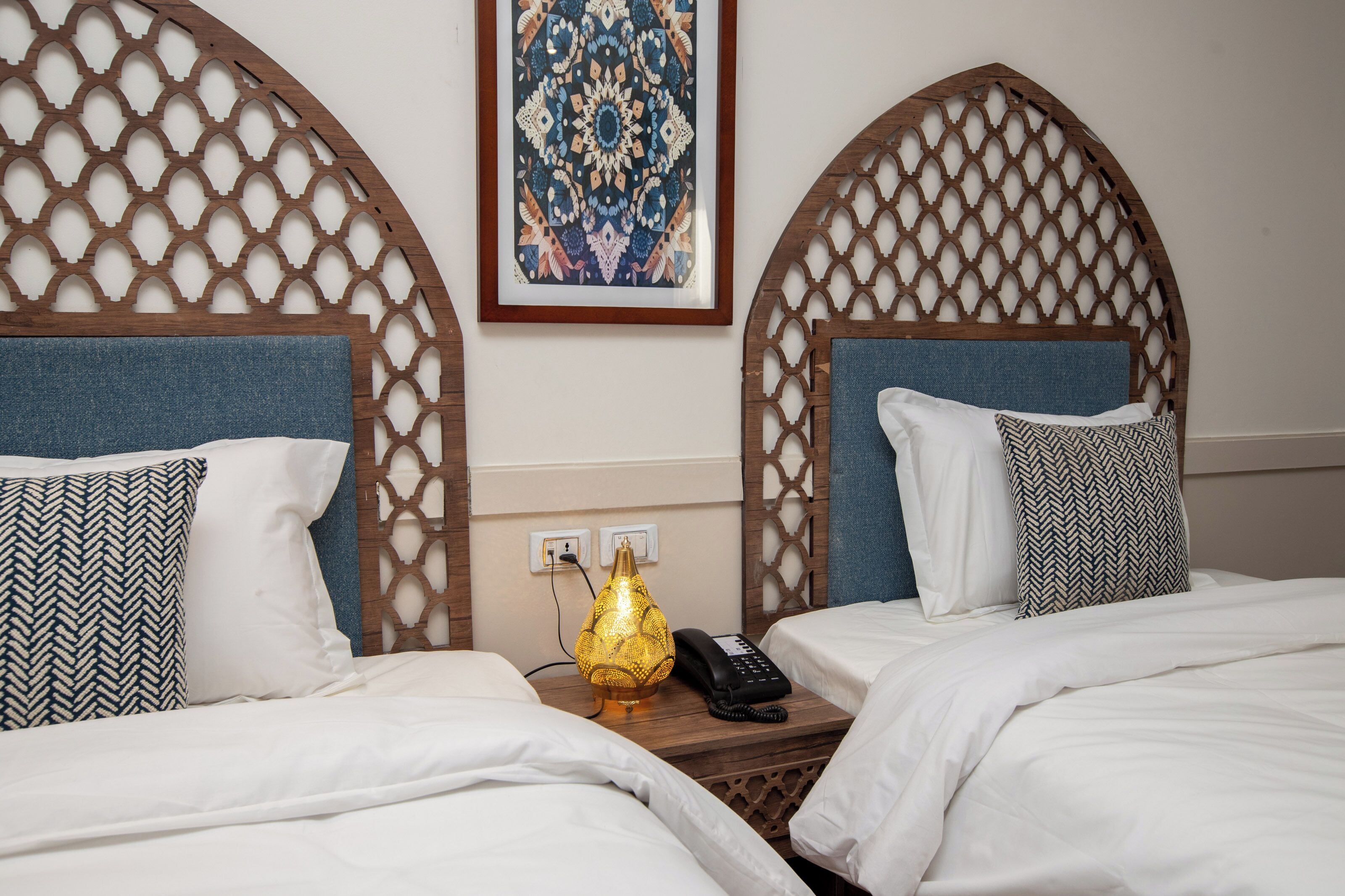 Habitación de hotel con dos camas, un tapiz decorativo, un enchufe y un teléfono en la mesita de noche.