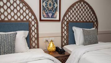 Habitación de hotel con dos camas, un tapiz decorativo, un enchufe y un teléfono en la mesita de noche.