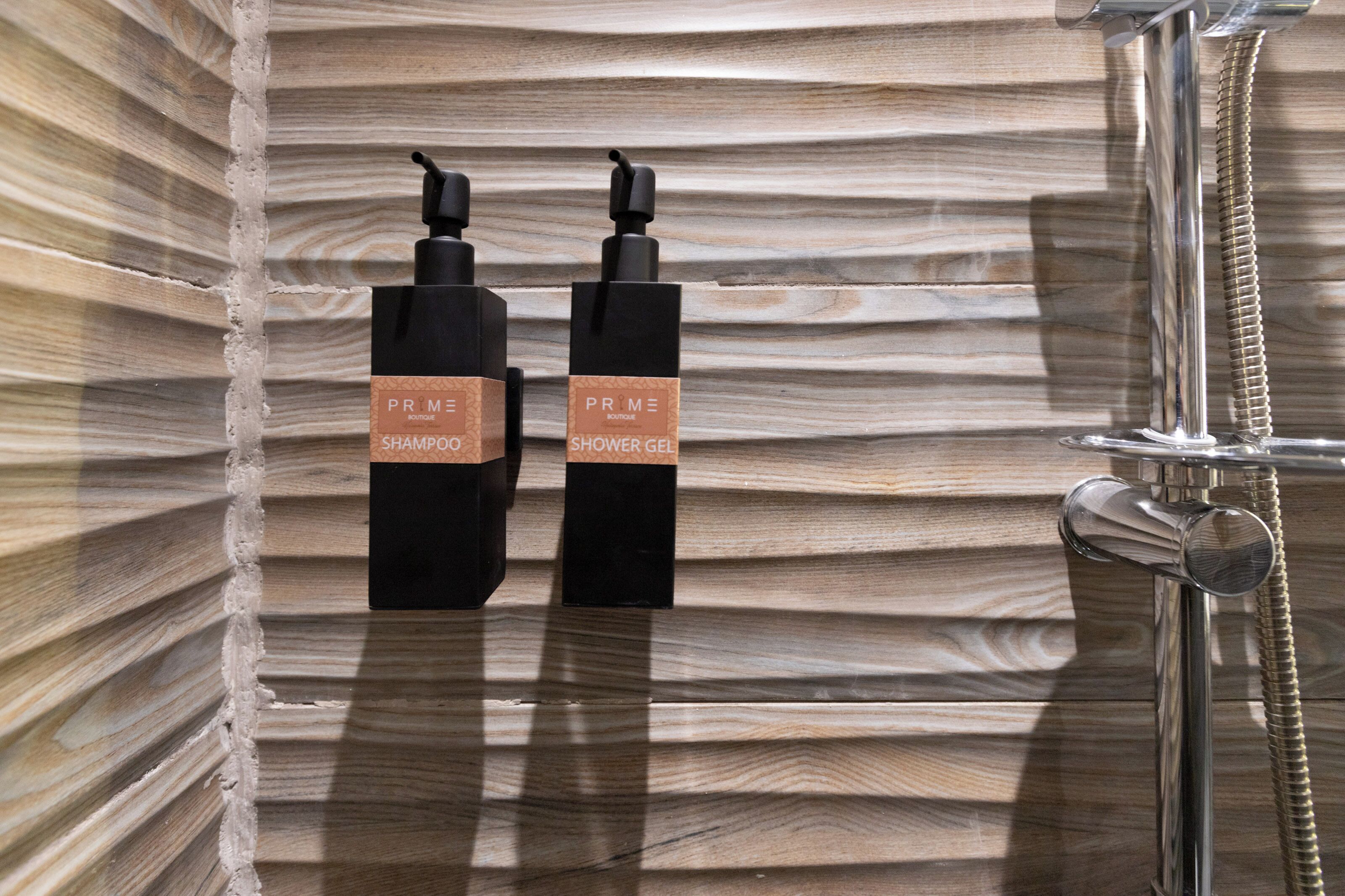 Deux bouteilles noires, portant des étiquettes, sont fixées à un mur en bois, à côté d’un pommeau de douche et d’un tuyau en métal.
