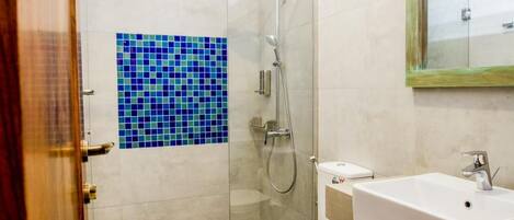 Un baño con cabina de ducha de vidrio, inodoro blanco, lavabo con espejo y pared de mosaicos azules.