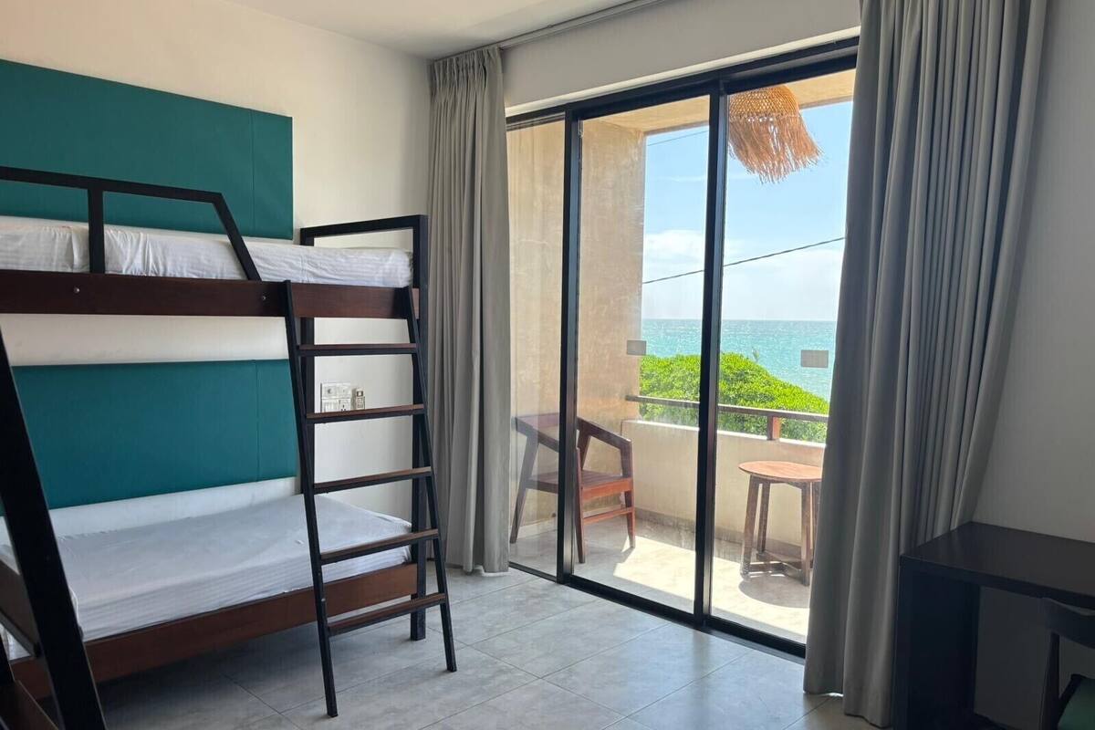 A room with a bunk bed, a small table, and a balcony with a view of the ocean.