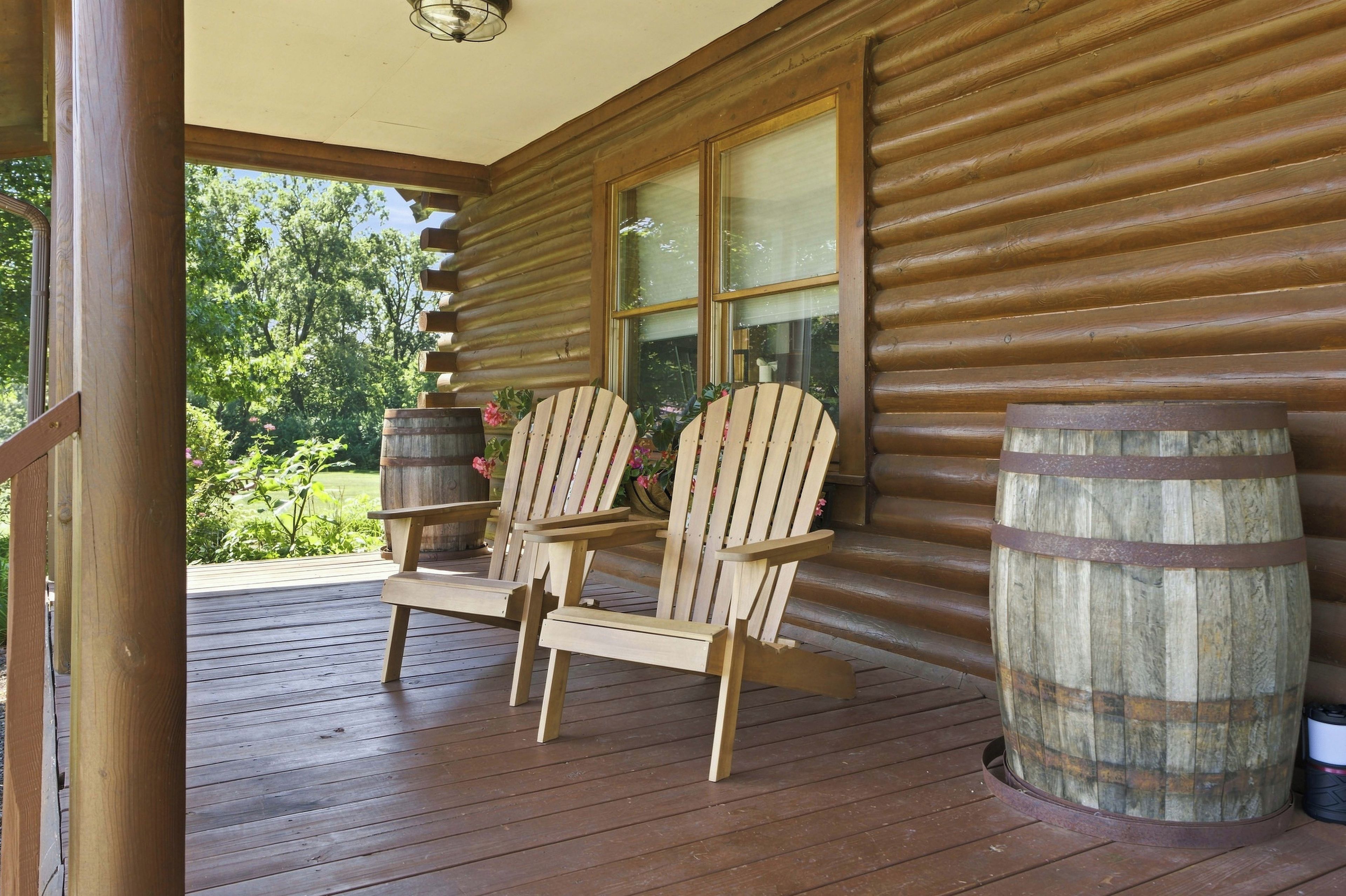 Eine Holzlaube mit Veranda, zwei Adirondack-Stühlen und zwei Holzfässern.