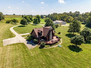 A large, single-story house with a wrap-around porch, surrounded by a well-maintained lawn and trees. - The Rec Farm - Log Cabin, Private Lake, Hot Tub, Arcade Barn, Sleeps 12+ (Shelbyville)