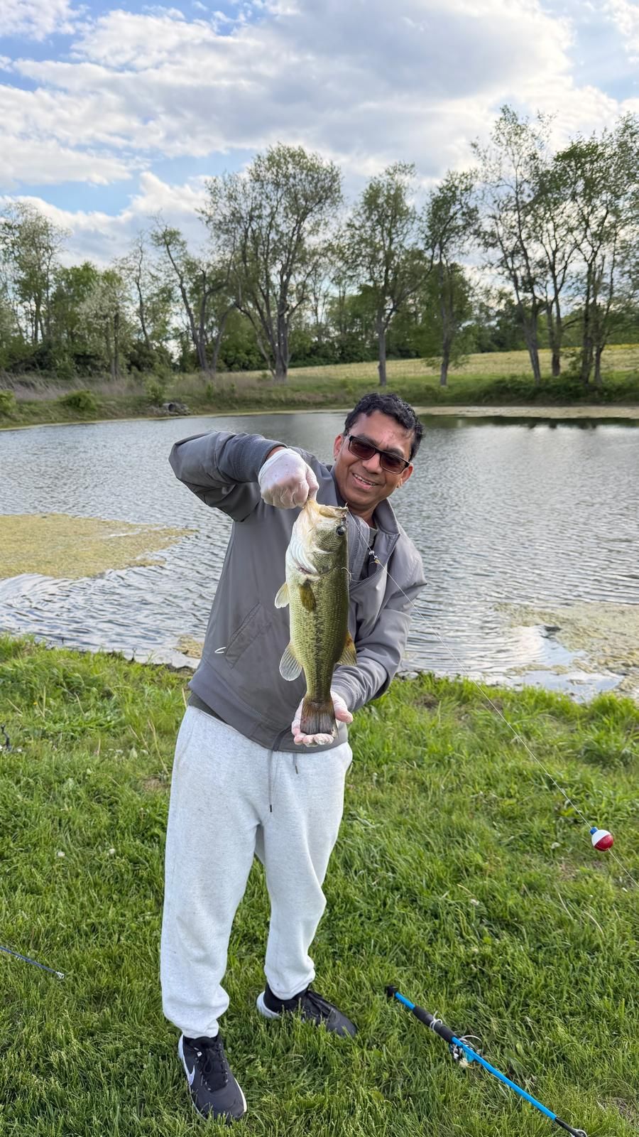 A person holding a fish near a body of water with grass and trees in the background.