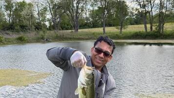 A person holding a fish near a body of water with grass and trees in the background.