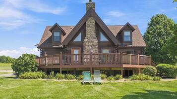 A log cabin with a stone chimney, a wooden deck, and a grassy yard.