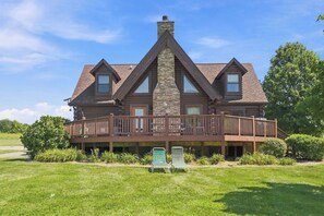 A log cabin with a stone chimney, a wooden deck, and a grassy yard. - The Rec Farm - Log Cabin, Private Lake, Hot Tub, Arcade Barn, Sleeps 12+ (Shelbyville)