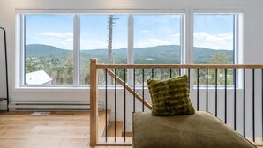 Een kamer met een houten leuning, een comfortabele zitting en een groot raam met uitzicht op een bergachtig landschap.