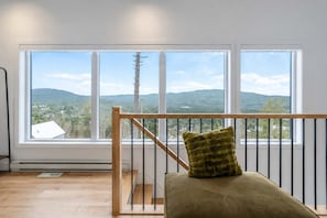 Una habitación con barandilla de madera, un asiento acolchado y un amplio ventanal con vistas a un paisaje montañoso.