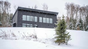 Een modern, donker gebouw met grote ramen, omgeven door met sneeuw bedekte grond en bomen.