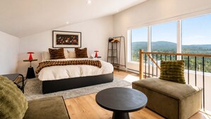 Een moderne slaapkamer met een groot bed, uitzicht op de omgeving en een balkon met een hekwerk.