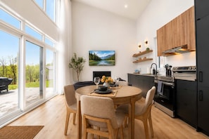 A modern kitchen with a dining area, large windows, and a view of the outdoors. - Modern Comfort | SPA | Mountain | Chalet KNOX (Saint-Côme)