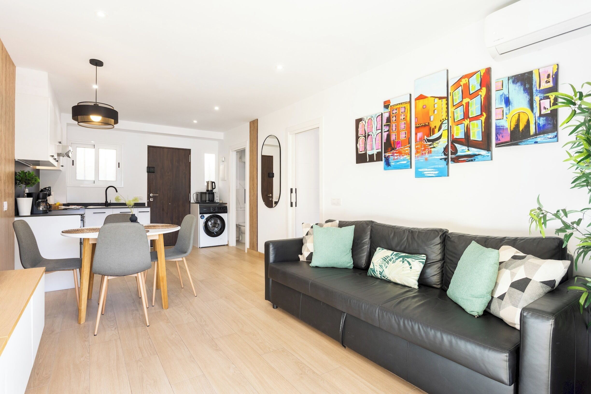 A modern living room with a black leather sofa, a dining table with chairs, and a kitchen in the background.