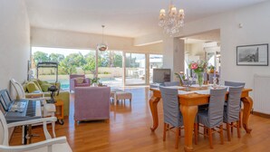 Amplia sala de estar con un piano, una mesa de comedor con sillas, un sofá y un ventanal con vistas al exterior.