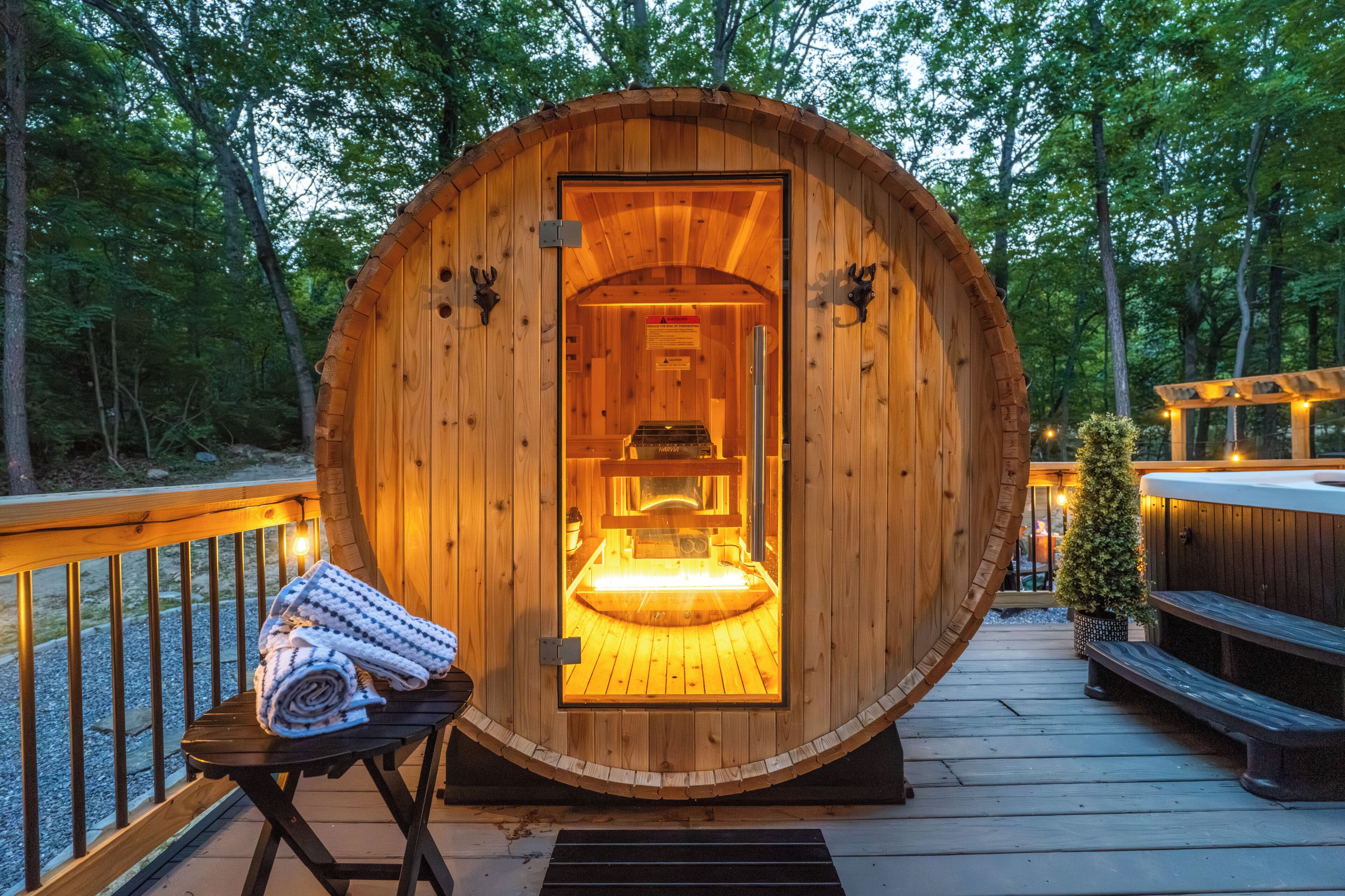 A wooden sauna with a bench outside, a bench inside, and a small tree in the background.