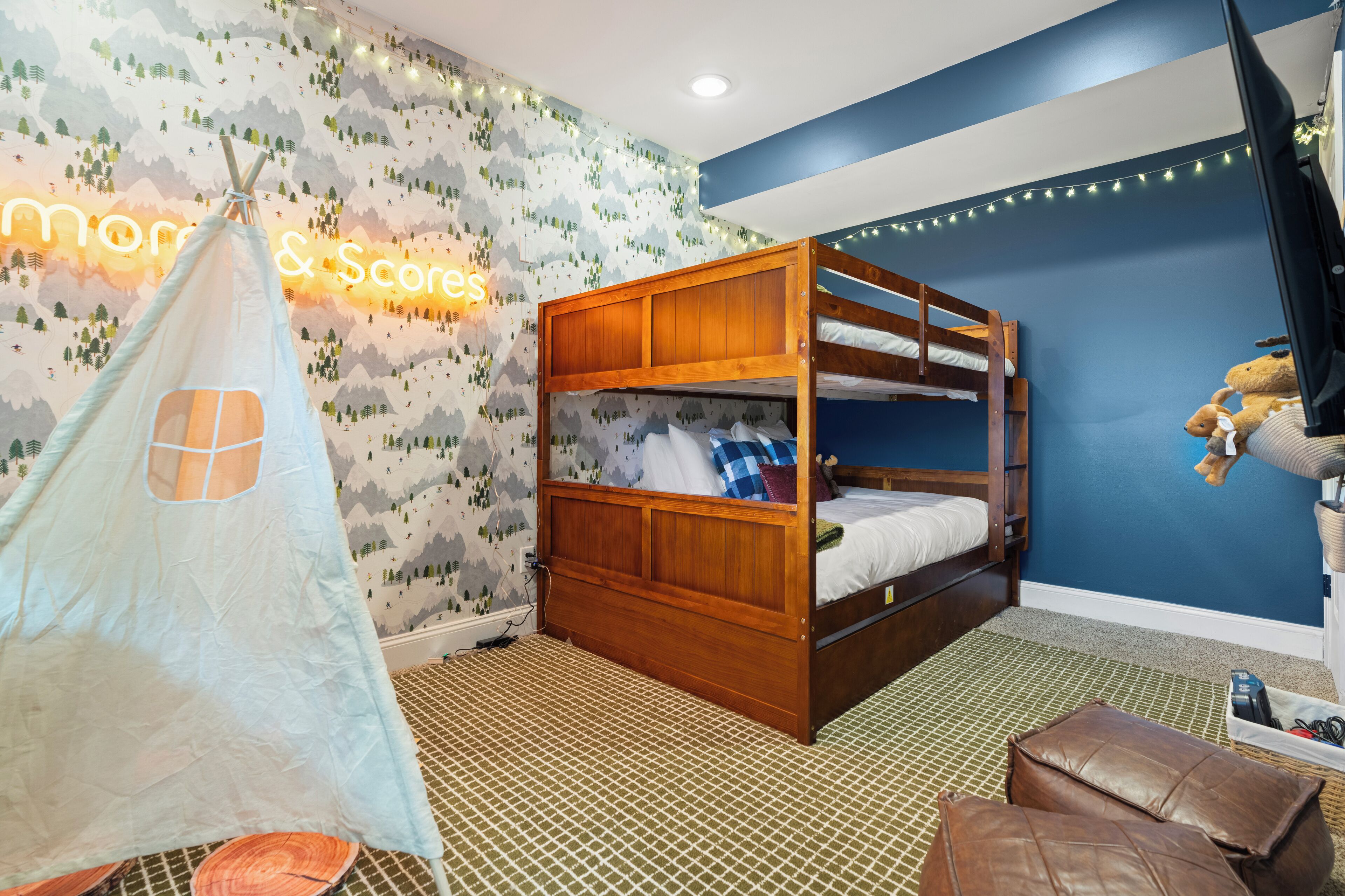 A bunk bed with a wooden frame and white bedding, a tent-like play area, and a wall with a mountain-themed wallpaper.