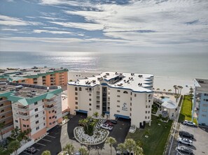 A multi-story hotel with a central courtyard, a pool, and a view of the ocean. - Beachfront Bliss with Gulf Views, Balcony, Heated Pool & More (Indian Shores)
