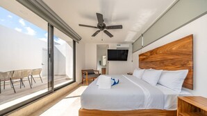 A modern hotel room with a large bed, a ceiling fan, a TV, and a balcony with chairs. - Tulum 2BR | Two Floors | Private Terrace + Grill (Tulum)