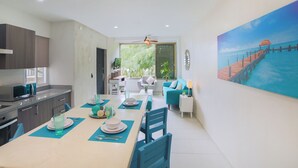 Een moderne keuken met donkere kasten, een eethoek met een tafel gedekt voor twee personen, en een groot schilderij van een pier boven water aan de muur.
