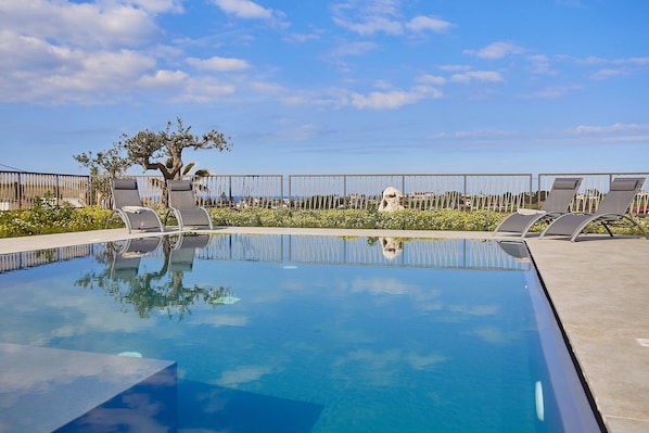 A clear blue pool with lounge chairs and a tree in the background.
