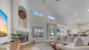 A spacious living room with a fireplace, large windows, and a modern kitchen in the background. - Beverly Ocotillo Chandler (Chandler)