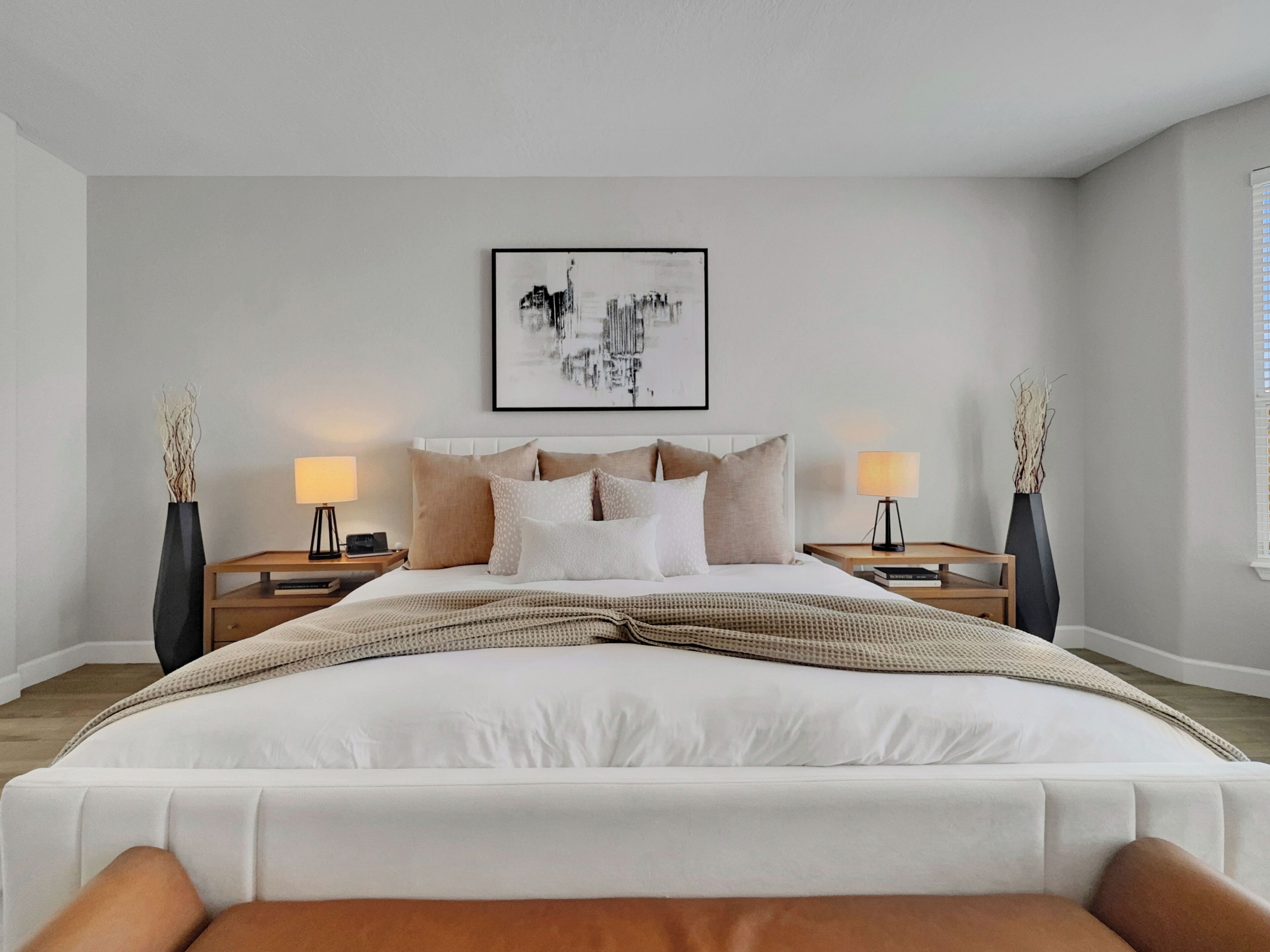 A modern bedroom with a large bed, two bedside tables, and a cityscape artwork on the wall.
