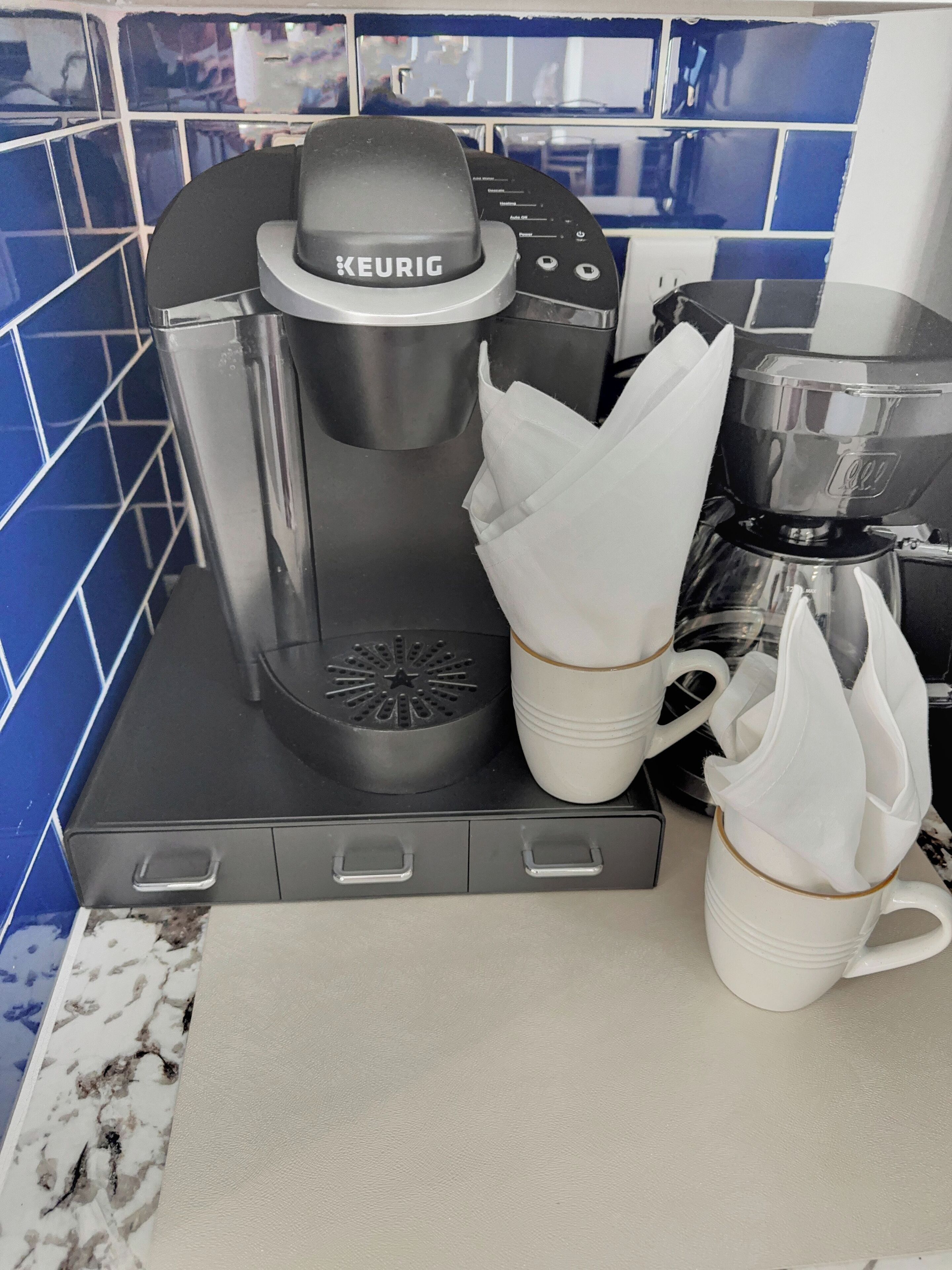 Una macchina per caffè Keurig con due tazze bianche e un serbatoio dell'acqua su un piano di lavoro della cucina.