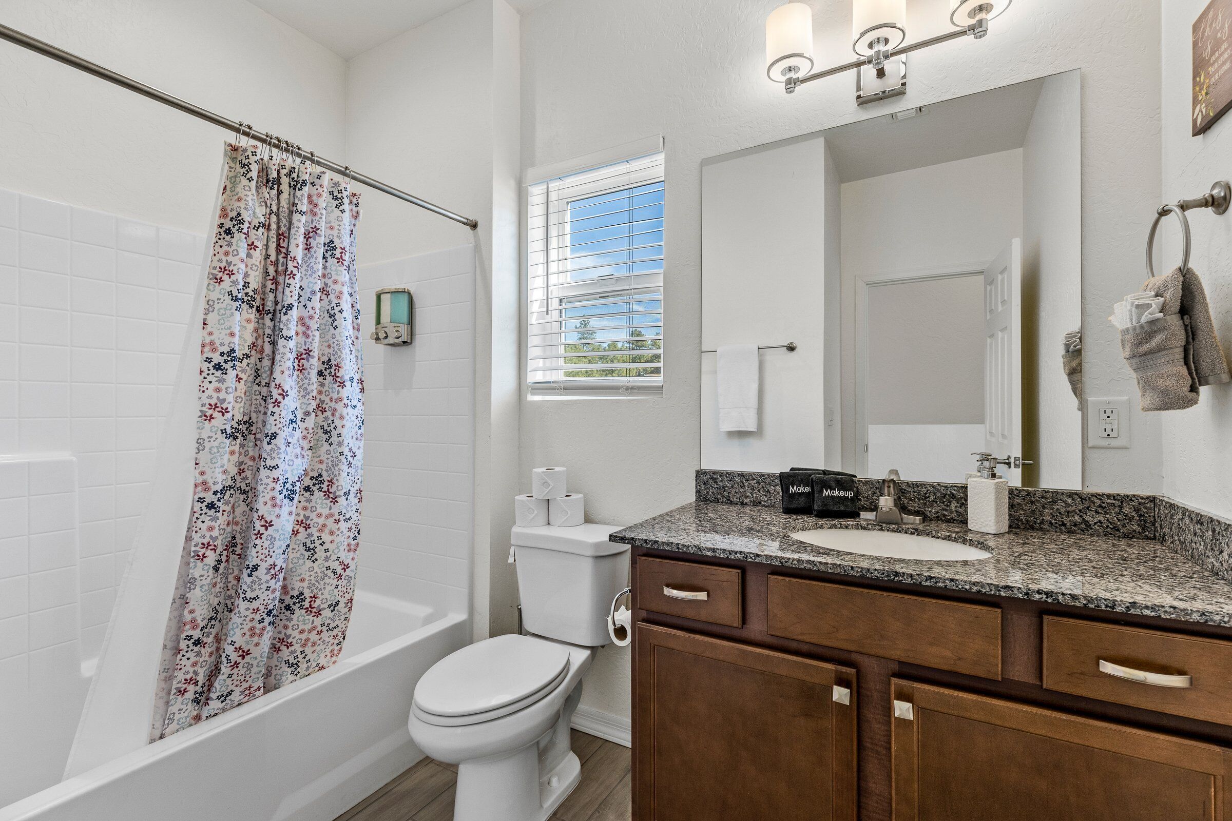 A bathroom with a shower, toilet, vanity, and a large mirror.