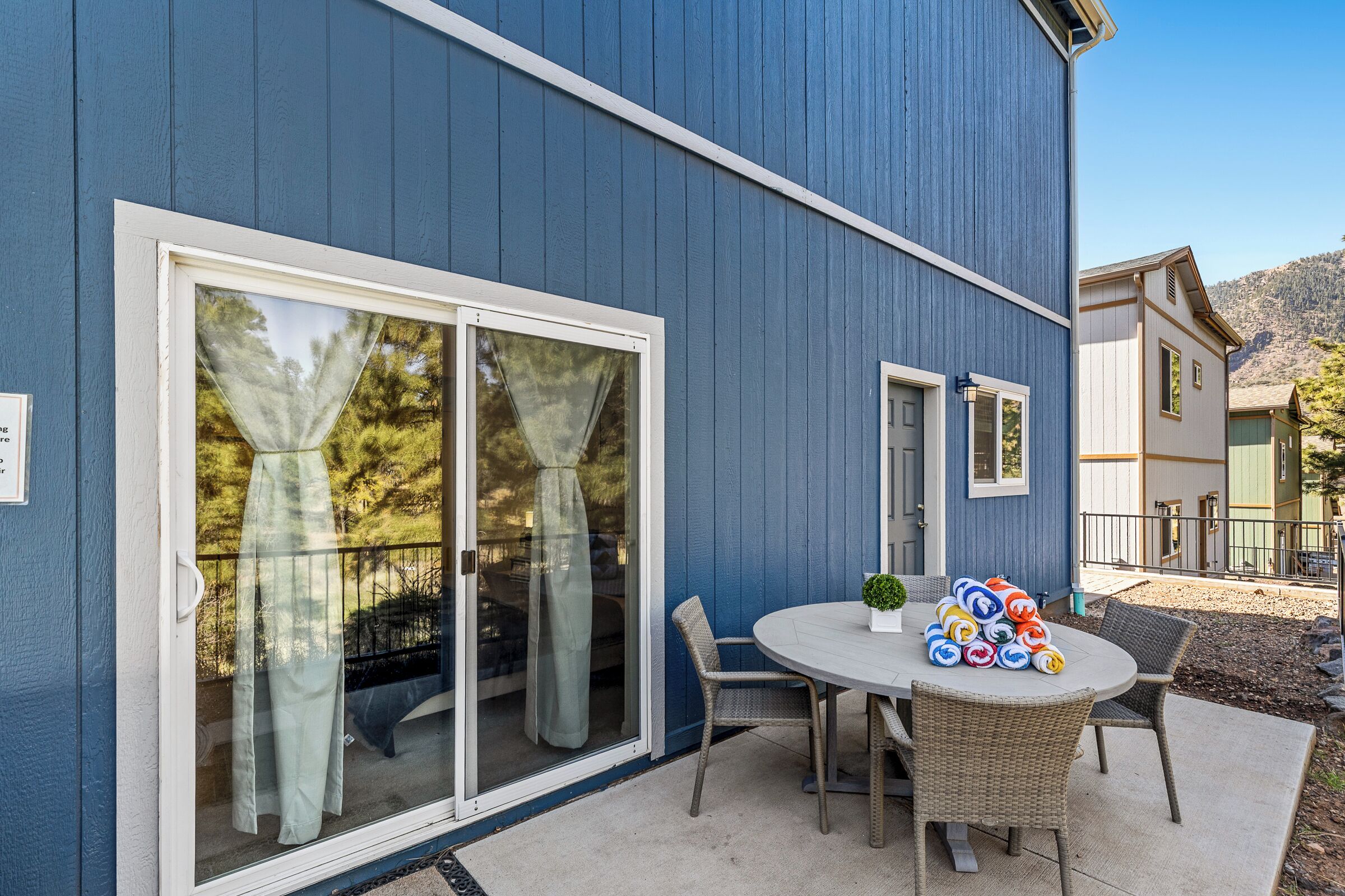 A blue building with a patio area featuring a table and chairs, a sliding glass door, and a small garden.