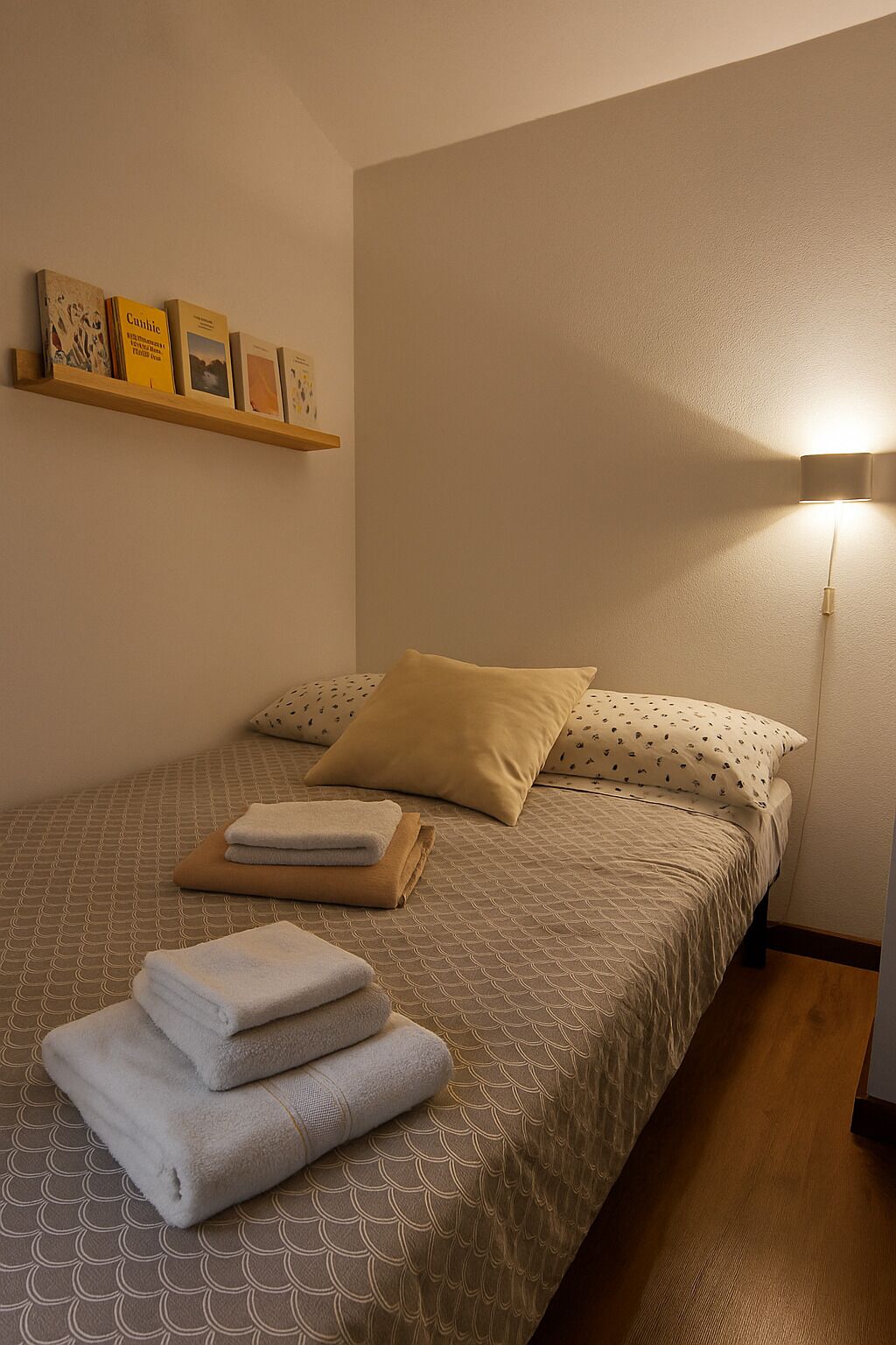 A neatly made bed with a patterned bedspread, two pillows, and folded towels on the bed.