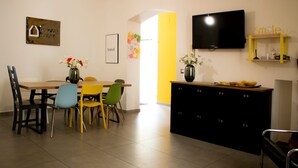 A dining area with a table and chairs, a television mounted on the wall, and a cabinet with numbered drawers. - Queen Room with Garden View, Shared Terrace, Wi-Fi and Air Conditioning (Vietri sul Mare)