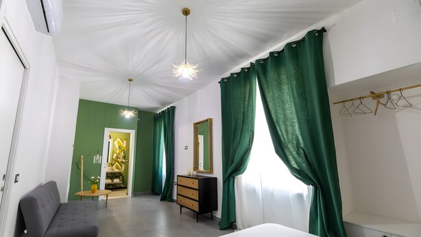 A bedroom with a bed, a dresser, a vanity, a mirror, a chair, and a hanging shoe rack. - Queen Room with Garden View, Shared Terrace, Wi-Fi and Air Conditioning (Vietri sul Mare)