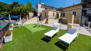 A rooftop with artificial grass, lounge chairs, and a blue car parked nearby. - Queen Room with Garden View, Shared Terrace, Wi-Fi and Air Conditioning (Vietri sul Mare)