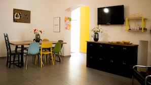 A dining area with a table and chairs, a television mounted on the wall, and a cabinet with numbered drawers. - Superior Triple Room with Shared Terrace, Wi-Fi and Air Conditioning (Vietri sul Mare)