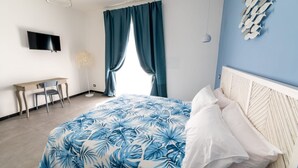 A bedroom with a bed, a desk, a chair, a TV, and a window with curtains. - Superior Triple Room with Shared Terrace, Wi-Fi and Air Conditioning (Vietri sul Mare)
