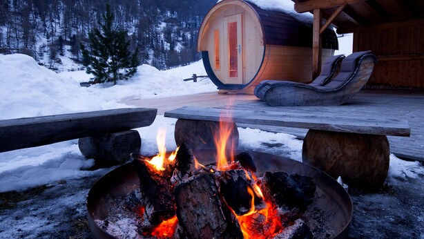 Une cabane en bois avec un foyer, un banc et un tonneau.