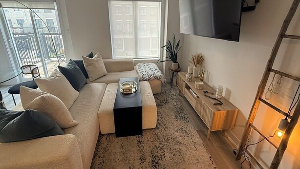 Ein modernes Wohnzimmer mit Ecksofa, Couchtisch, Wand-Fernseher und einer Holzkommode.