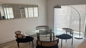 Ein moderner Essbereich mit einem runden Glastisch, vier schwarzen Stühlen und einer hohen Stehlampe.