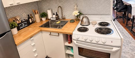 A modern kitchen with white cabinets, a black and white tiled backsplash, a stainless steel sink, and a white stove with four burners.