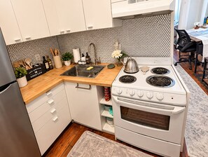 A modern kitchen with white cabinets, a black and white tiled backsplash, a stainless steel sink, and a white stove with four burners. - Heart of OTR -Stadiums, Museums, Nightlife, Casino -Walkable Everywhere Cinci (Cincinnati)
