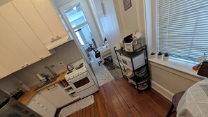 A compact kitchen with white cabinets, a stove, and a microwave. There's a small dining area with a table and chairs, and a window with blinds. - Heart of OTR -Stadiums, Museums, Nightlife, Casino -Walkable Everywhere Cinci (Cincinnati)