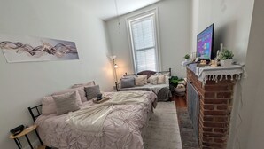 A bedroom with two beds, a brick fireplace, a desk, and a large window. - Heart of OTR -Stadiums, Museums, Nightlife, Casino -Walkable Everywhere Cinci (Cincinnati)