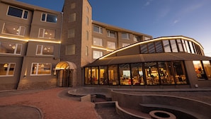 A modern hotel with a curved glass facade, a brick entrance, and a courtyard with seating areas. - Hotel Rosario Uyuni Collection (Uyuni)