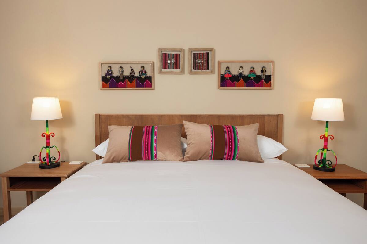 A hotel room with a large bed, two bedside tables with lamps, and three framed pictures on the wall.