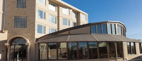 Un edificio moderno con fachada de vidrio curva, torre de ladrillo y una entrada amplia con puerta de cristal.