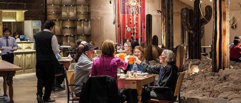 Een restaurantinterieur met een groep mensen aan een tafel, een ober in de buurt, en een bar op de achtergrond.