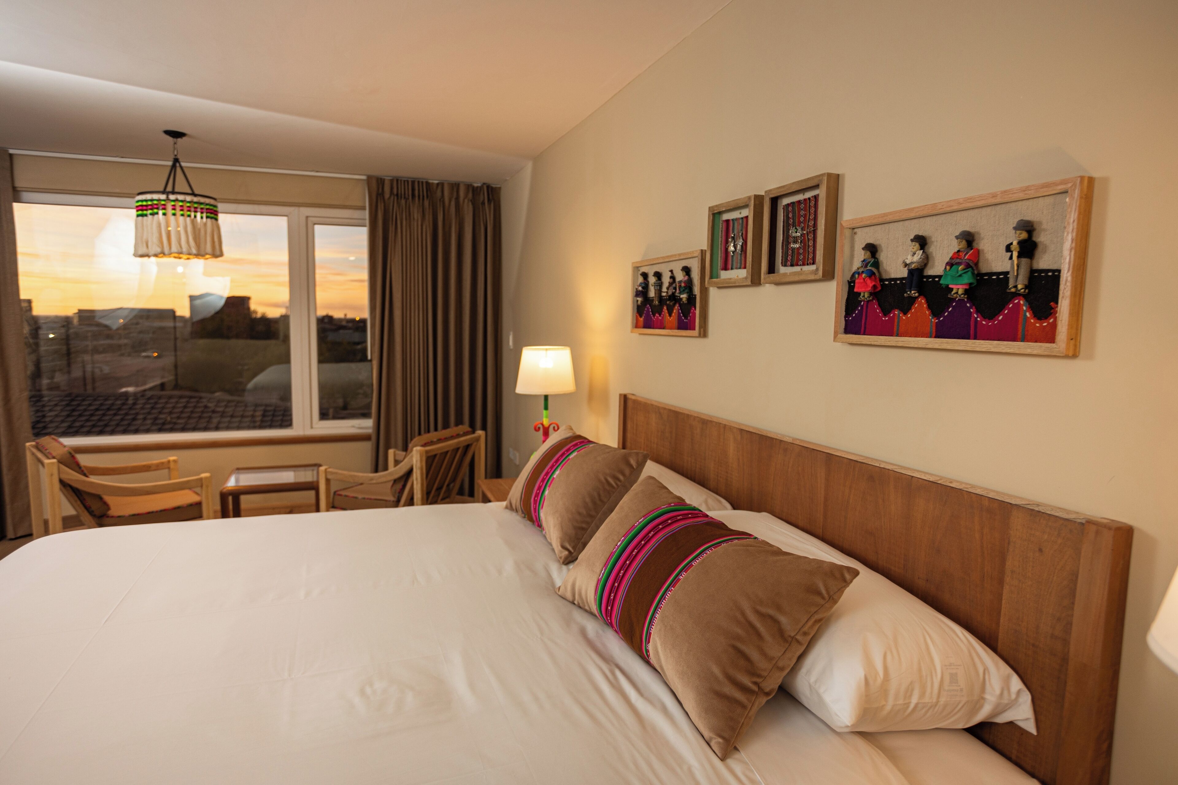 A hotel room with a large bed, a desk, a chair, a window with curtains, and wall-mounted artwork.